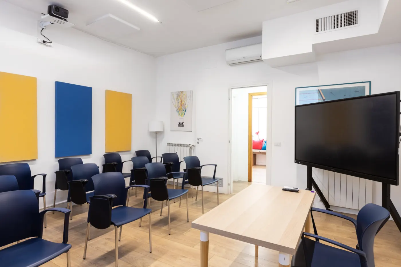 Un’aula con le sedie blu, i pannelli colorati alle pareti e lo schermo per le lezioni